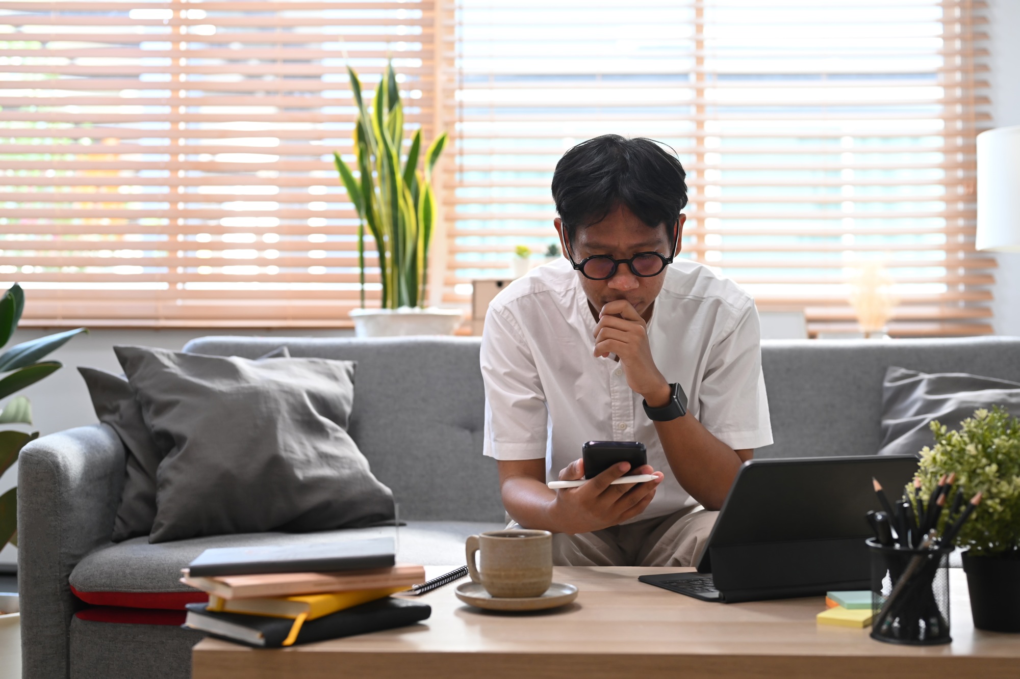 Man sitting on couch in living room and using smart phone for shopping online.